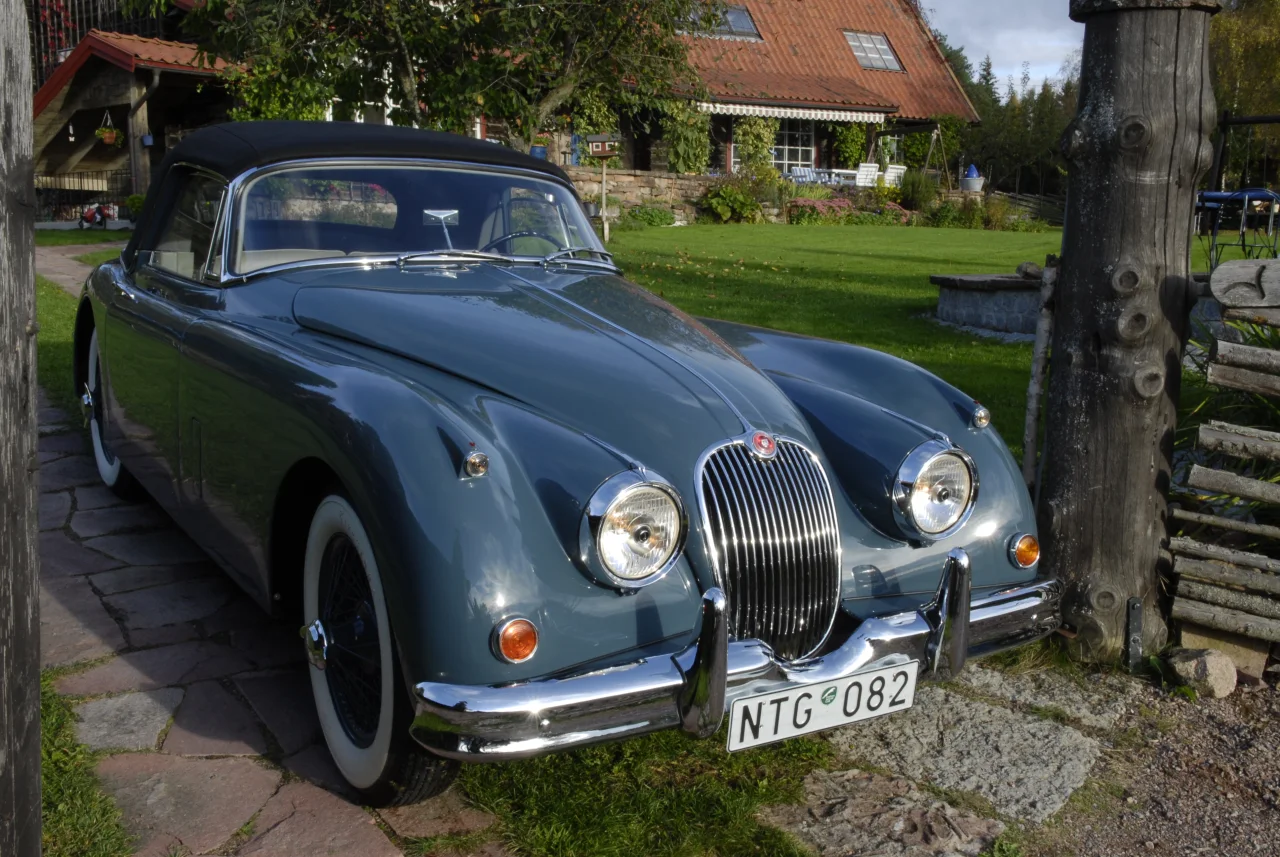 XK150 parkerad vid en trädgårdsgrind med den svarta suffletten uppfälld