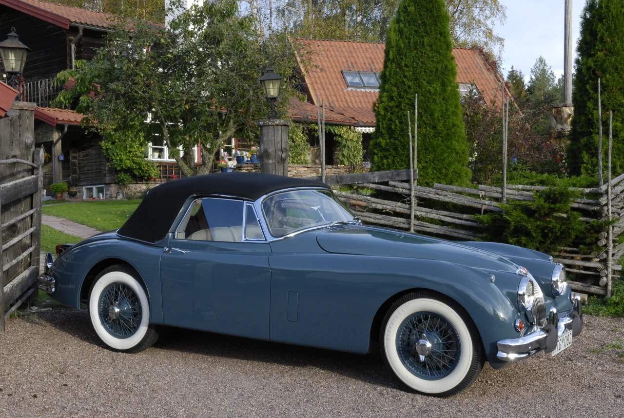 XK150 i profil vid ett trästaket med suffletten uppfälld