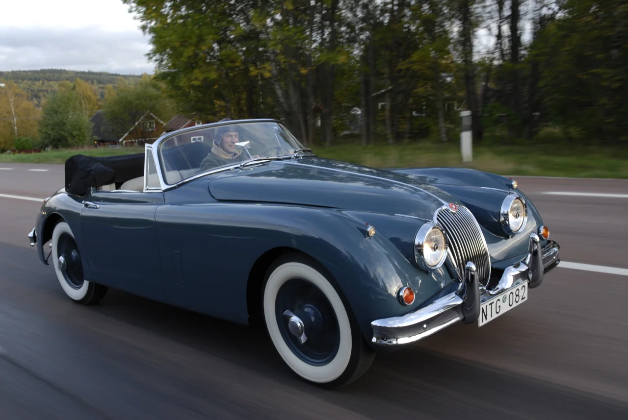 XK150 med nedfälld sufflett under färd, snett framifrån från motsatt sida